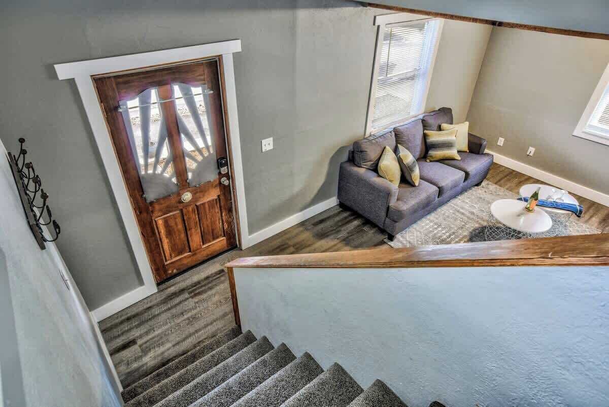 Un escalier menant à un salon avec un canapé gris et une porte en bois.