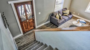 Un escalier menant à un salon avec un canapé gris et une porte en bois.