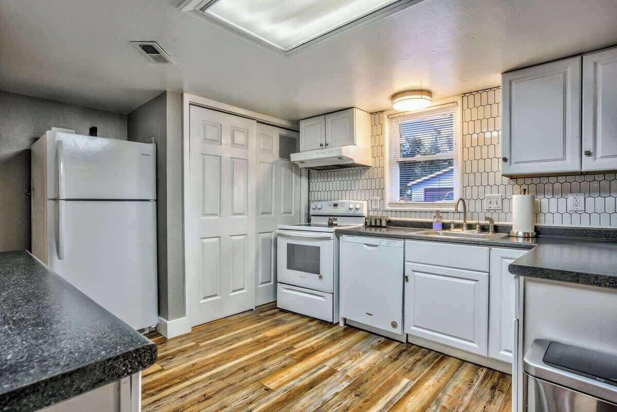 A kitchen with white cabinets, a wooden floor, and a window with blinds.