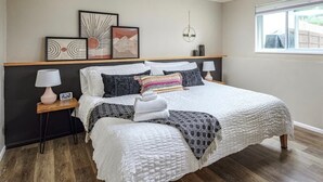 Une chambre à coucher avec un grand lit, une table de chevet, une commode, une lampe fixée au mur et des œuvres d’art accrochées au mur.