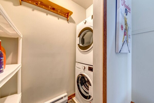 Un cuarto de lavado con lavadora y secadora, un estante de madera y un cartel en la pared.