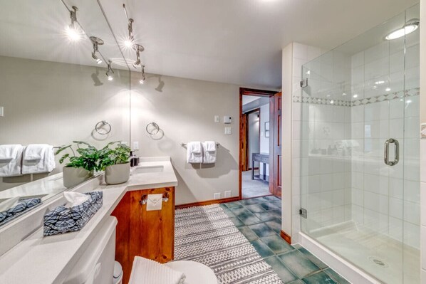 Un baño moderno con cabina de ducha de vidrio, tocador de madera y un espejo grande.