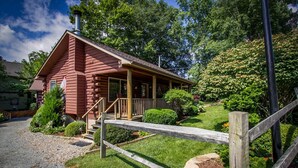 Une cabane en rondins dotée d’un porche, entourée d’une clôture en bois et d’une végétation luxuriante.