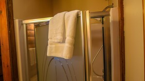 Une cabine de douche fermée par des parois de verre, avec une serviette blanche accrochée à la porte.