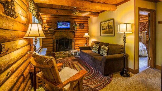 L’intérieur d’un chalet confortable, avec une cheminée, des murs en bois, un canapé, un fauteuil et un téléviseur.