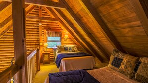 A cozy attic bedroom with a wooden sloped ceiling, a bed with a blue blanket, and a window with curtains. - Queen Bedroom with Loft (Blowing Rock)
