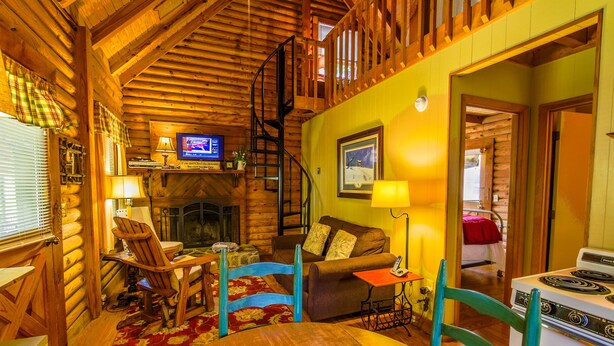 A cozy cabin interior with a wooden dining table, blue chairs, a sofa, a fireplace, and a kitchen area with a stove. - Queen Bedroom with Loft (Blowing Rock)