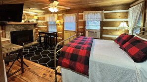 A cozy cabin room with a bed, a fireplace, a desk, and a ceiling fan. - Queen Cozy Cabin on Main St (Blowing Rock)