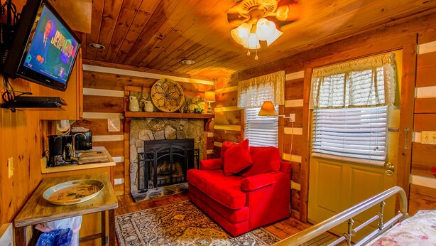 A cozy cabin interior with a fireplace, a red sofa, a television, and a wooden ceiling. - Queen Cozy Cabin on Main St (Blowing Rock)
