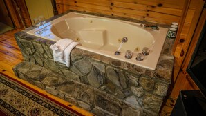 A stone-floored bathtub with a white interior, a towel draped over the edge, and a glass set on the side.