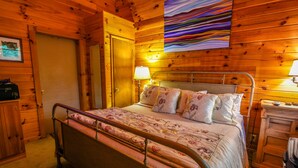 A wooden cabin bedroom with a metal bed frame, a bedside table with a lamp, and a wooden wardrobe.