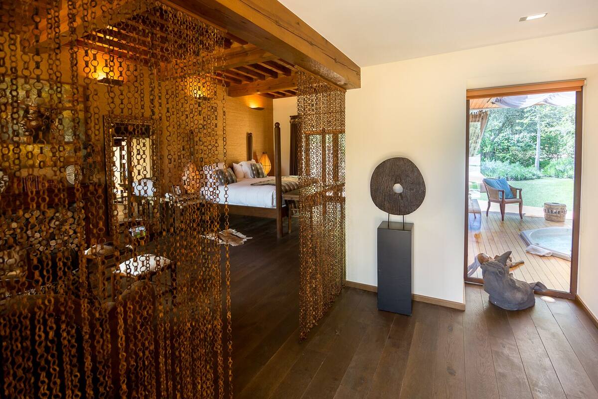 A bedroom with a bed, a wooden ceiling, and a view of a garden through a glass door.