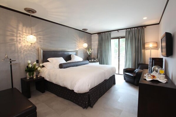 A modern hotel room with a large bed, bedside tables, a desk with breakfast items, and a view of the outdoors.