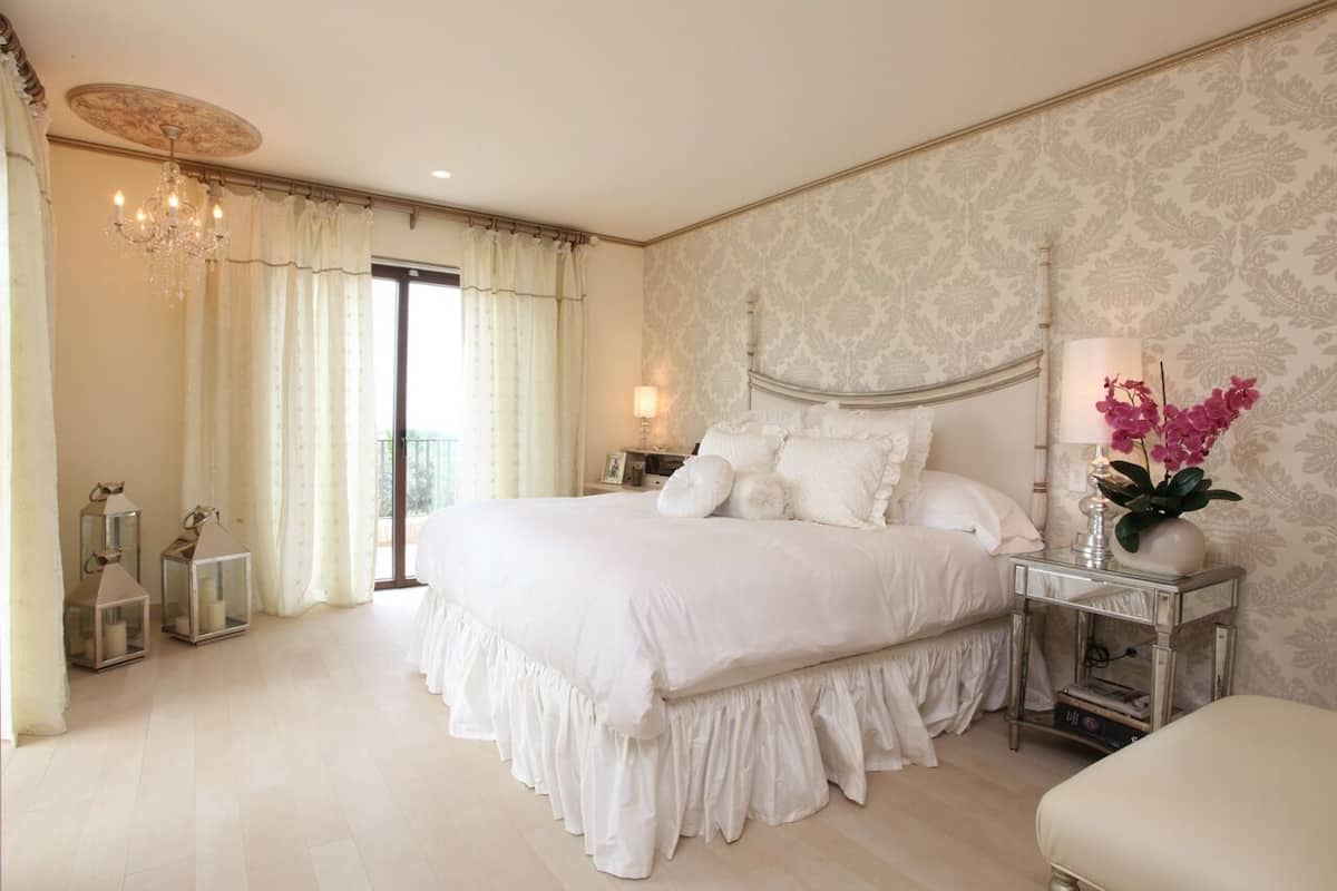 A spacious bedroom with a large bed, a chandelier, and a view of the outdoors.