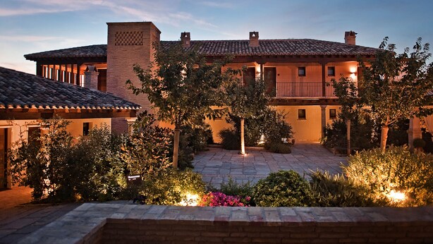 A large, multi-story building with a courtyard, featuring a tiled roof, brick walls, and outdoor lighting. - Hotel Cigarral de las Mercedes (Toledo)