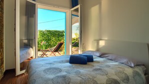 A bedroom with a bed, pillows, and a view of a garden through an open door. - Two Bedroom Apartment with Pool, Jacuzzi, A/C, WiFi and Electric Bicycles (Bordighera)