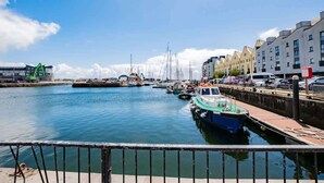 Un puerto deportivo con barcos amarrados a lo largo de la costa, edificios al fondo y un cielo despejado.