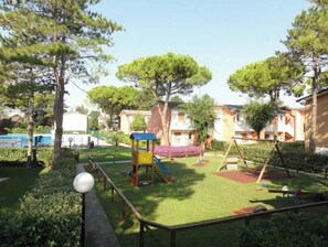 Children can play on the slide and swings in this safe, shaded outdoor area surrounded by mature trees and residential buildings.