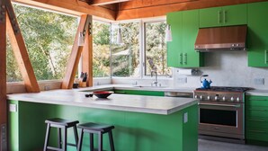 A modern kitchen with green cabinets, a large island with stools, a stove, and a view of trees through large windows. - Modern Retreat 15 minutes from Healdsburg Square (Healdsburg)