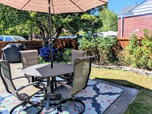 Een terras met een ronde tafel, vier stoelen, een parasol en een barbecue.