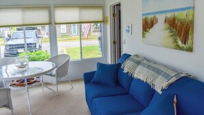 Una habitació amb un sofà blau, una taula de vidre i un quadre d'un camí a la platja.