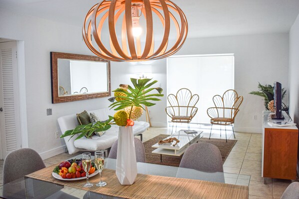 Un salon moderne comprenant un coin repas, des meubles blancs, un grand miroir et un luminaire suspendu original.