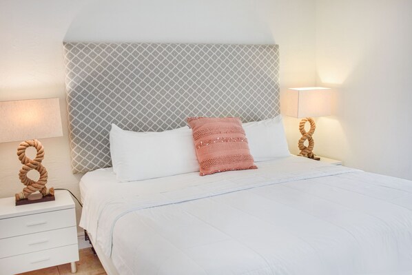 Una cama bien hecha con ropa blanca y una única almohada decorativa.