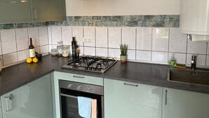 Une cuisine équipée d’une cuisinière à gaz, d’un four et d’un crédence recouverte de carreaux bleus. On y trouve des placards, un évier et une plante en pot posée sur le plan de travail.