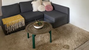 Un salon moderne avec un canapé d’angle gris foncé, une table basse ronde et un tapis à poils longs de couleur beige.