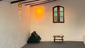 Une pièce avec un plafond en pente, une fenêtre avec un cadre en bois, une petite table avec des bougies et une pile d’objets cylindriques verts.