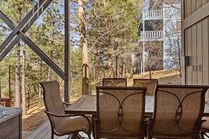 A dining area with a table and chairs, a hot tub, and a view of trees and a building.