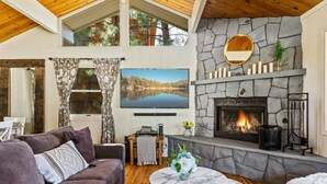 Un salon chaleureux avec une cheminée en pierre, un canapé confortable, un téléviseur et une vue sur un lac, visible à travers de grandes fenêtres.
