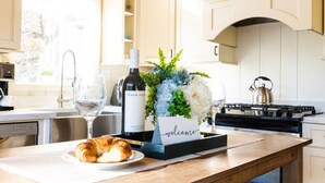 Une cuisine avec une table en bois, une bouteille de vin, un bouquet de fleurs, une pancarte « Bienvenue » et un croissant sur une assiette.