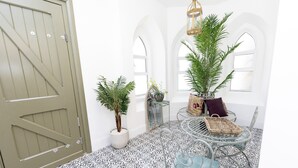 Um quarto com piso estampado, uma mesa redonda com cadeiras, um vaso de planta e uma porta grande.