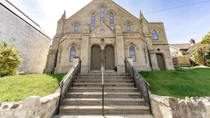 Uma igreja de pedra com entrada central, uma torre de sino e uma escadaria que leva à entrada.