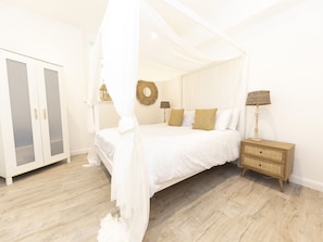 Ein Schlafzimmer mit Himmelbett, Kleiderschrank, Nachttisch und Wandlampe.