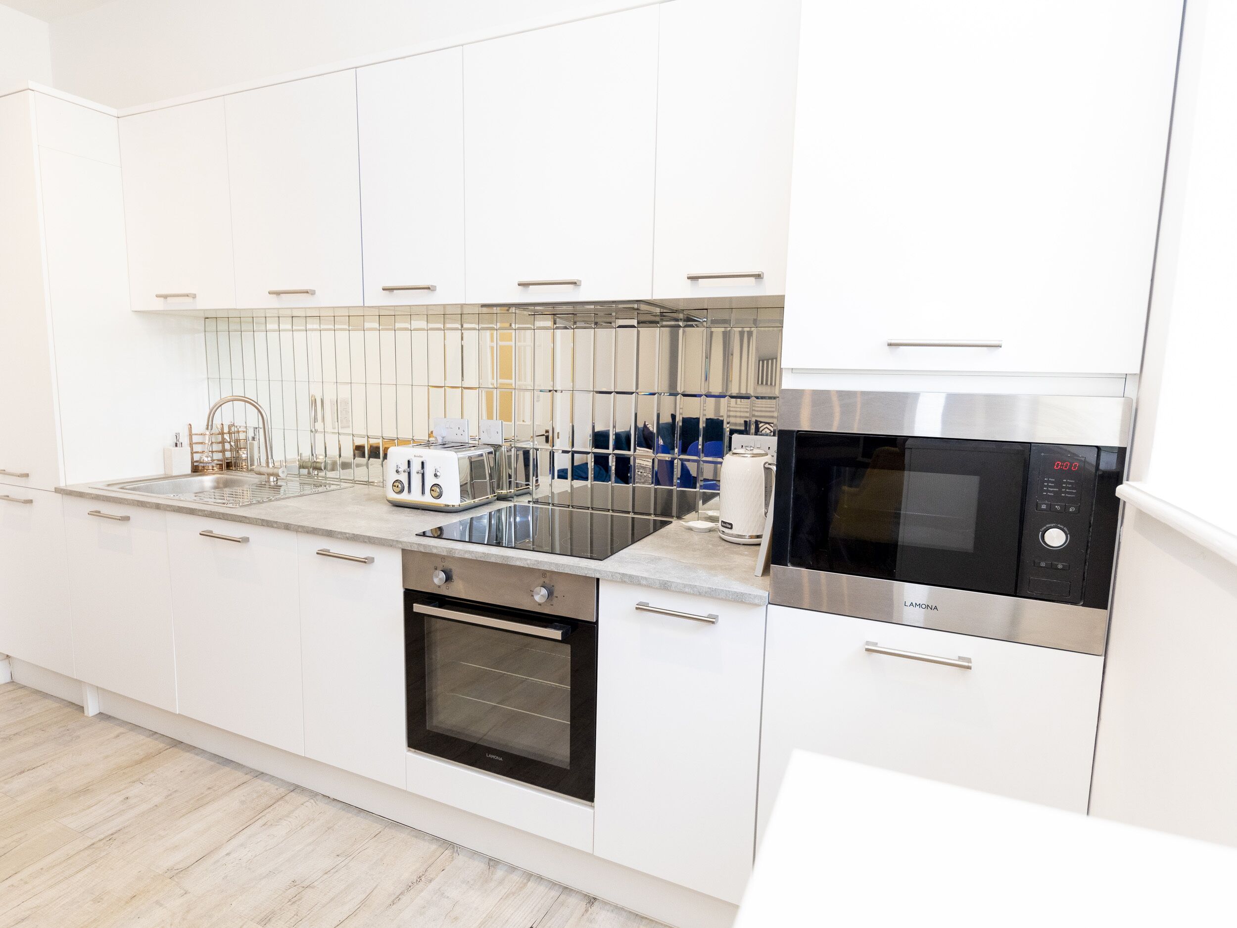 Une cuisine moderne avec des meubles blancs, un four encastré, un four à micro-ondes et un grille-pain.