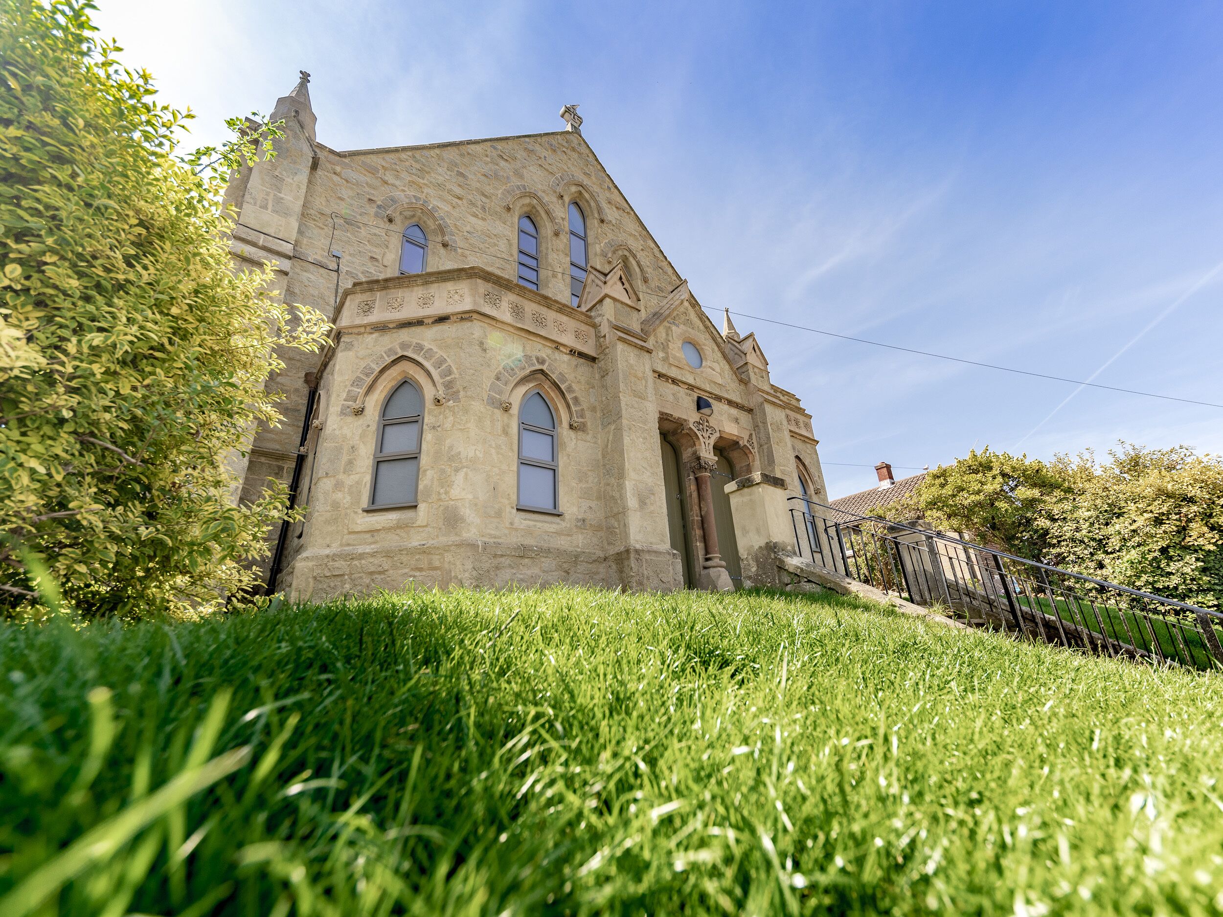 A stone building with arched windows and a central entrance, surrounded by greenery.