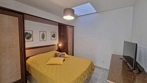 Un dormitorio con cama, televisor sobre un soporte de madera y cuadros en la pared.