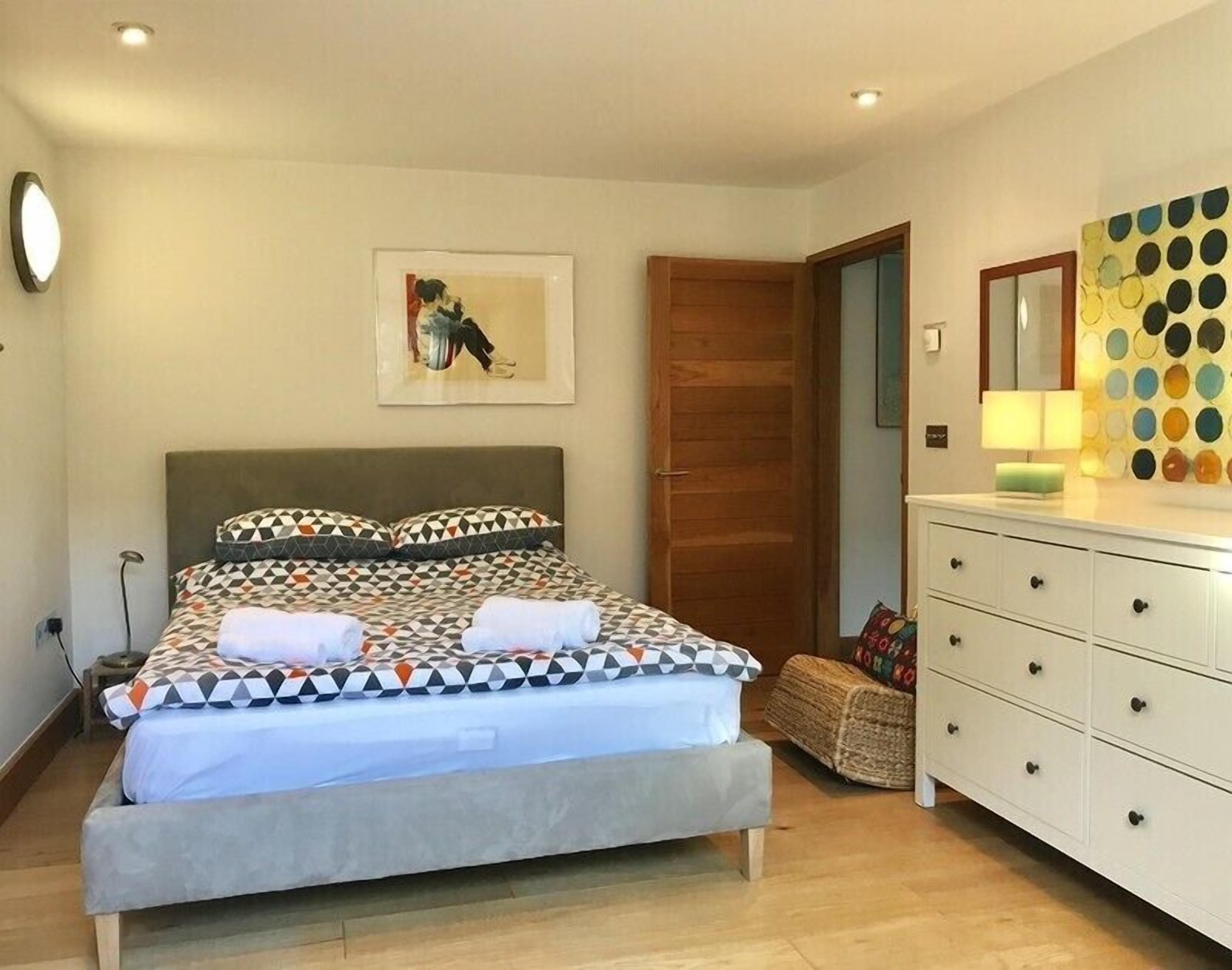 A bedroom with a bed, a dresser, a mirror, and a wall-mounted artwork.