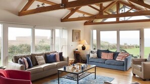 A spacious living room with high ceilings and exposed beams, large windows offering a view of the outdoors, and a cozy seating area with sofas and a coffee table.