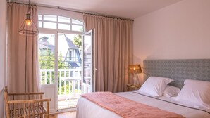 Un dormitorio con cama, mesita de noche, lámpara, silla y vista al exterior.
