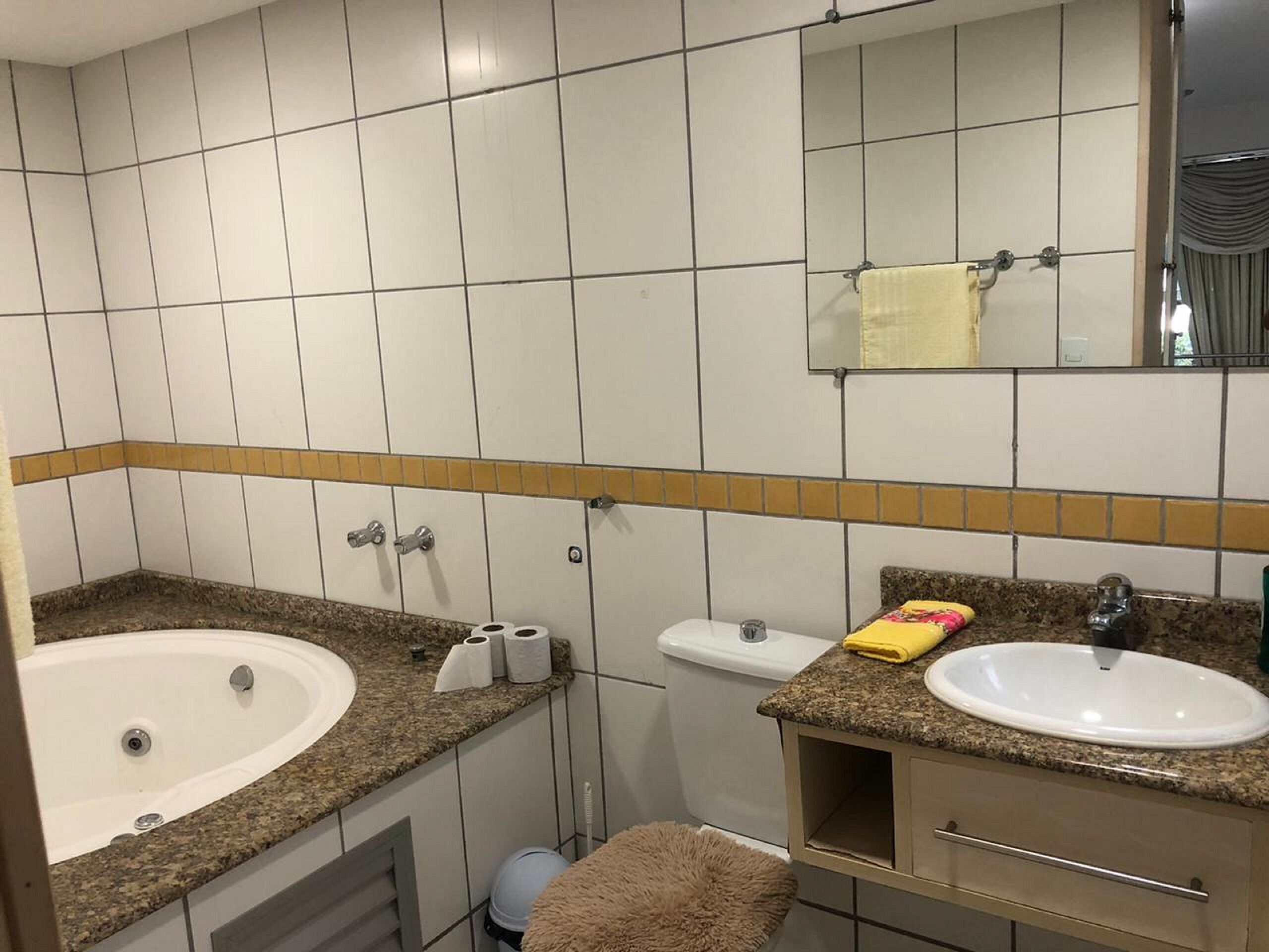 Un baño con una bañera, un lavamanos y un inodoro. Hay toallas y papel higiénico en la encimera.