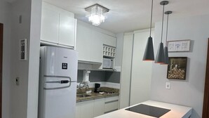 Een moderne keuken met witte kasten, een ingebouwde magnetron, een roestvrijstalen koelkast, een granieten aanrecht en hangende lampen.