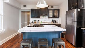 Una cocina moderna con una isla central, muebles oscuros, electrodomésticos de acero inoxidable y una lámpara colgante.
