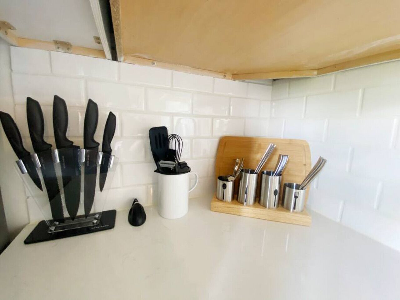 A kitchen with white tiled backsplash, a knife block, a coffee maker, and a utensil holder.