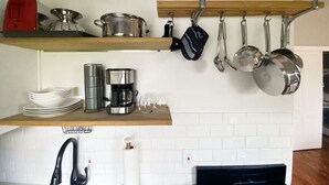 Eine Küche mit einer Holzablage, auf der Töpfe, Pfannen, eine Kaffeemaschine und gestapelte Teller stehen.