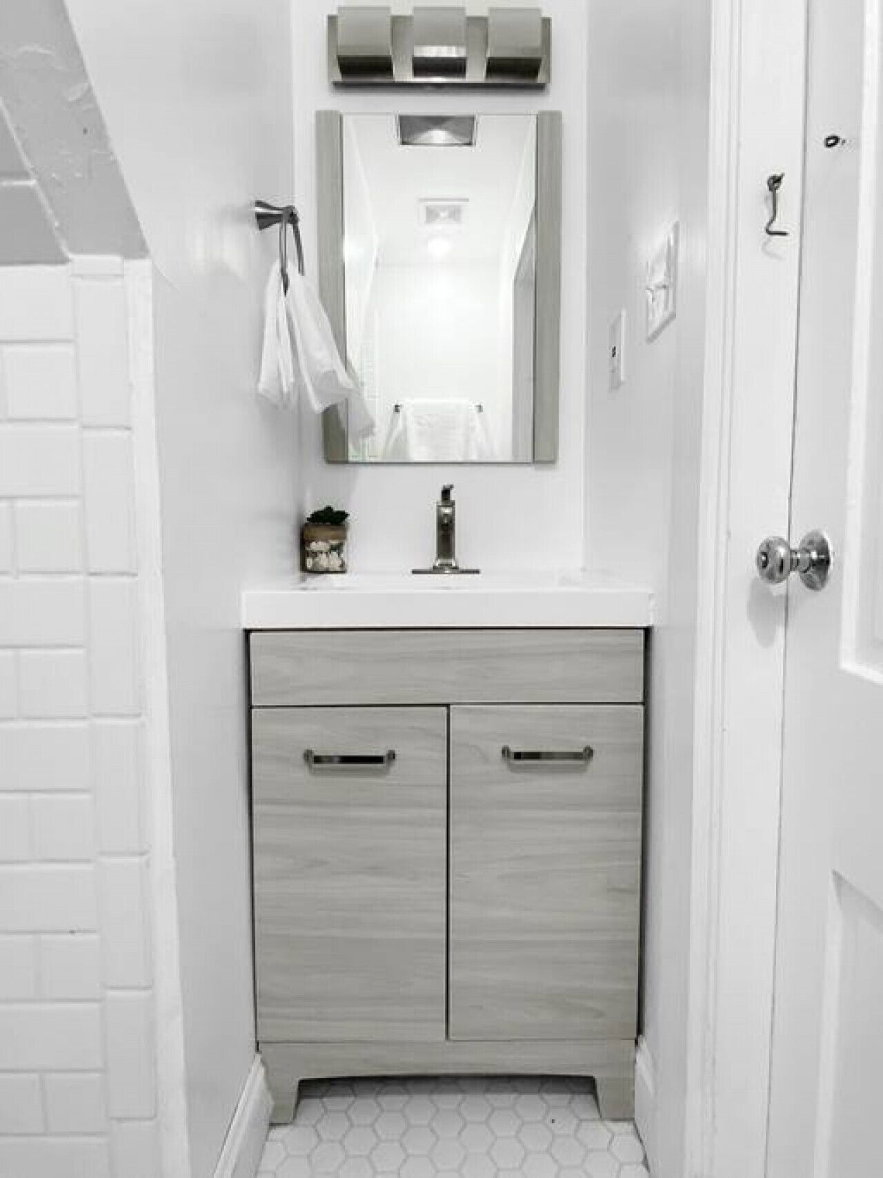 A bathroom with a white vanity, a mirror, and a door.