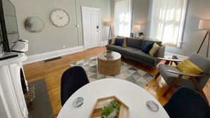 Ein Wohnzimmer mit grauem Sofa, einem weißen Couchtisch und einem Essbereich mit weißem Tisch und Stühlen.