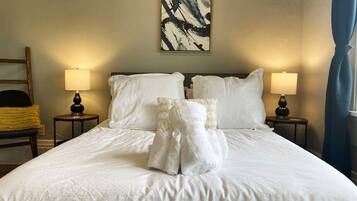 A neatly made bed with white linens and towels, two bedside lamps, and a painting on the wall.